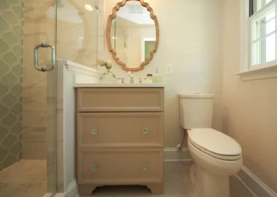 Custom bathroom renovation by Oak Ridge Builders with a gold mirror, simple vanity and glass shower.