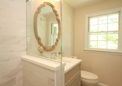 View of a renovated bathroom by Oak Ridge Builders with a glass shower, gold mirror, and neutral vanity