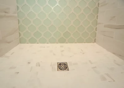 View up close of the white tile floor inside the shower with a light blue/green teal tile on the wall behind.