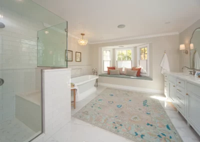 Bathroom renovation by Oak Ridge Builders with a window seat, bath tub, and glass shower with a rug in the middle of the space.