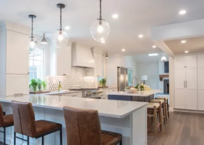 View of a coffee / breakfast corner facing into a renovated kitchen with a blue island and clear pendant lighting